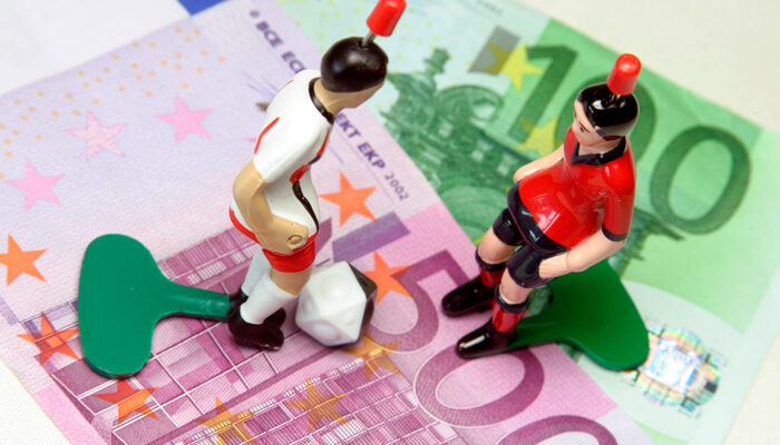 2 poppetjes met een alarm op hun hoofd staan op geldbiljetten. Ze symboliseren het aan banden leggen van gokken.