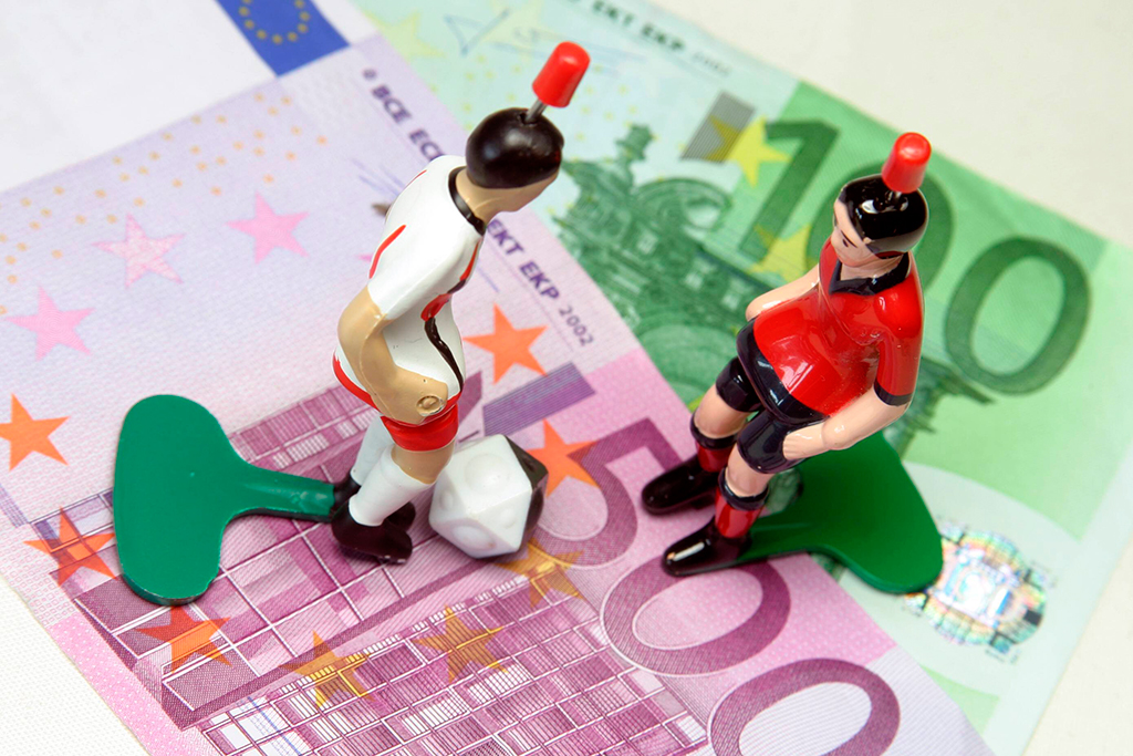 2 poppetjes met een alarm op hun hoofd staan op geldbiljetten. Ze symboliseren het aan banden leggen van gokken.