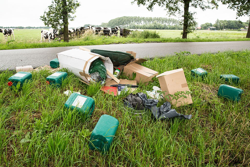 In een berm liggen diverse vaten met chemisch afval.