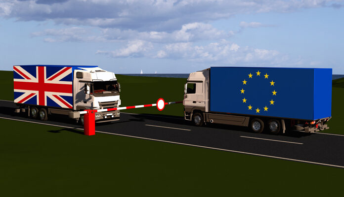 Twee vrachtwagens voor slagboom. Een vrachtwagen met vlag van UK, een vrachtwagen met vlag van EU