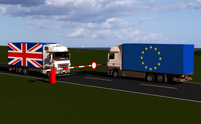 Twee vrachtwagens voor slagboom. Een vrachtwagen met vlag van UK, een vrachtwagen met vlag van EU