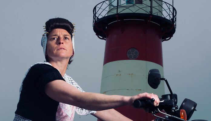 Vrouw in klederdracht op motor bij vuurtoren