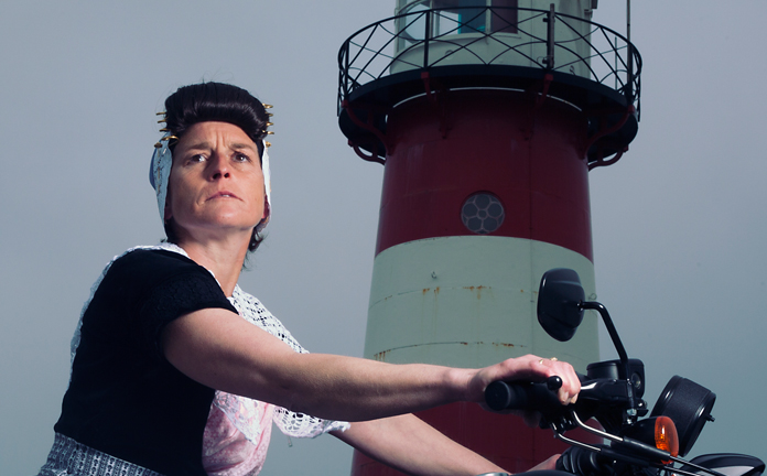 Vrouw in klederdracht op motor bij vuurtoren