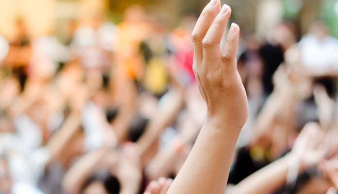 Iemand in zaal steekt hand op