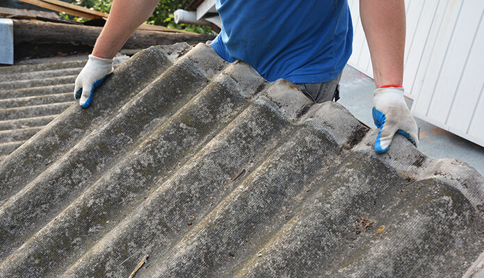 Iemand verwijdert met handschoenen asbestdak