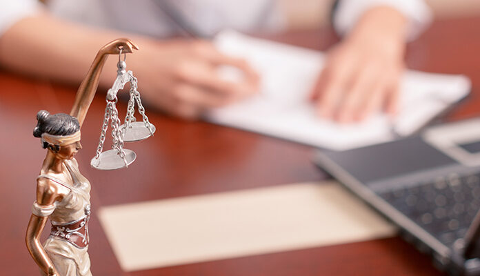 Afbeelding van vrouwe justitia met op de achtergrond iemand die formulieren invult