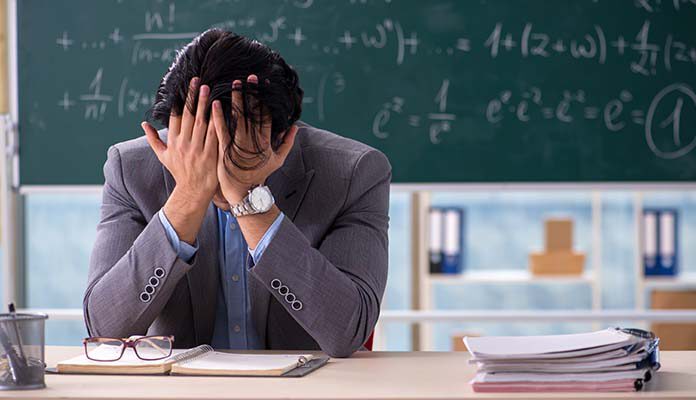 Meester zit voor het schoolbord en heeft handen in het haar