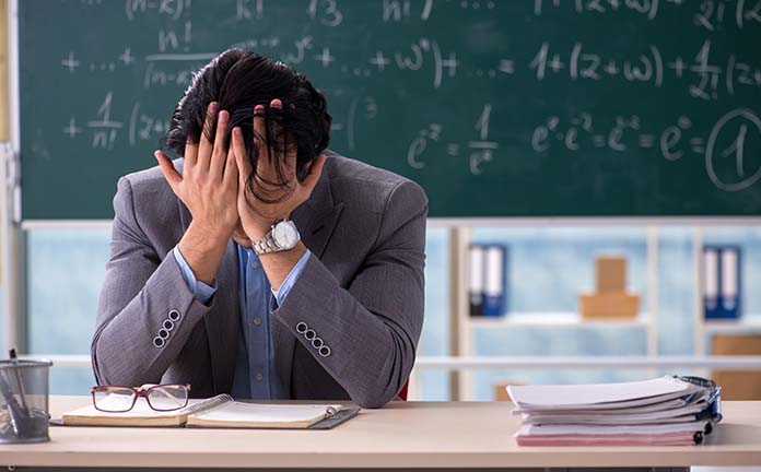 Meester zit voor het schoolbord en heeft handen in het haar
