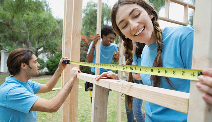 Drie personen bouwen een huis. Twee personen meten iets op.