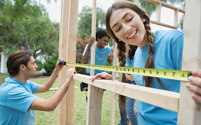 Drie personen bouwen een huis. Twee personen meten iets op.