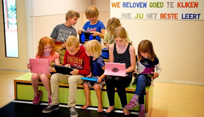 Kinderen bekijken hun ipads. Op de muur staat de tekst: 'We beloven goed te kijken hoe jij het beste leert.'
