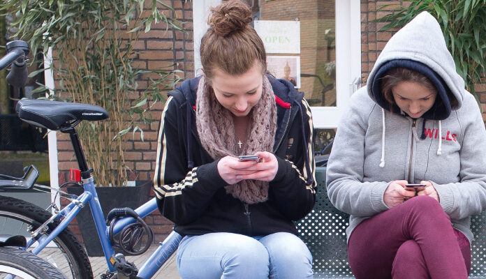 Twee meisjes op een bankje kijken op hun telefoon