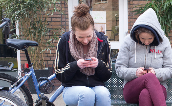 Twee meisjes op een bankje kijken op hun telefoon