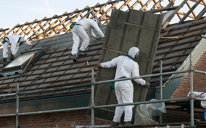 Mannen in speciale pakken verwijderen asbest van een dak.