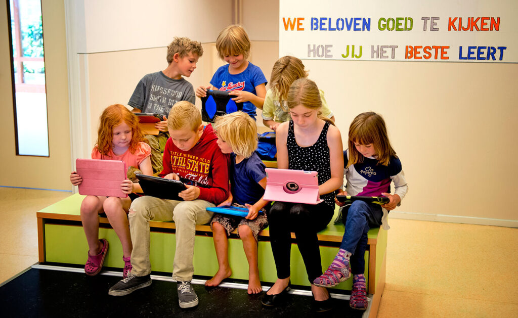 Kinderen bekijken hun ipads. Op de muur staat de tekst: 'We beloven goed te kijken hoe jij het beste leert.'