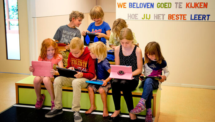 Kinderen bekijken hun ipads. Op de muur staat de tekst: 'We beloven goed te kijken hoe jij het beste leert.'