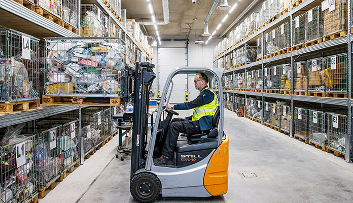 Douanemedewerker haalt met heftruck pallet met pakketjes uit stelling