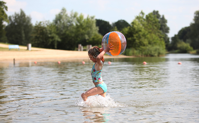 Klein meisje speelt met een bal in natuurwater.