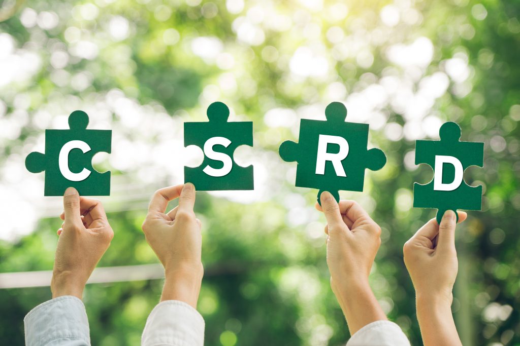 Vier handen houden allemaal een puzzelstukje met een letter vast, samen vormt dit de letters CSRD