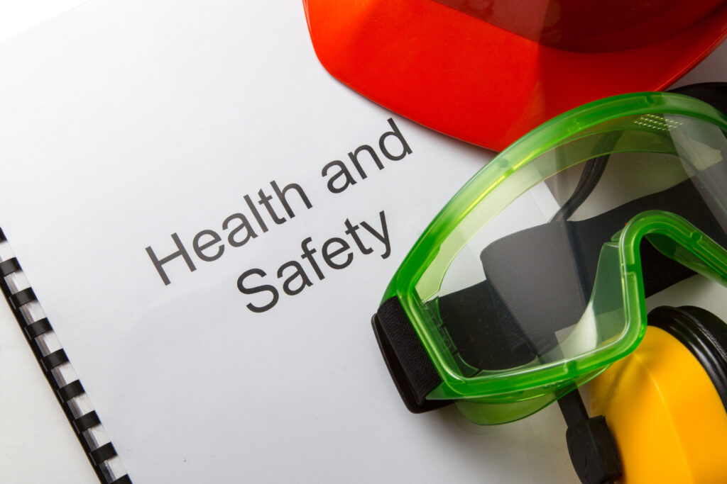 Rapport met daarop de tekst Health and Safety en daarnaast een veiligheidsbril, hem en oorbeschermers.